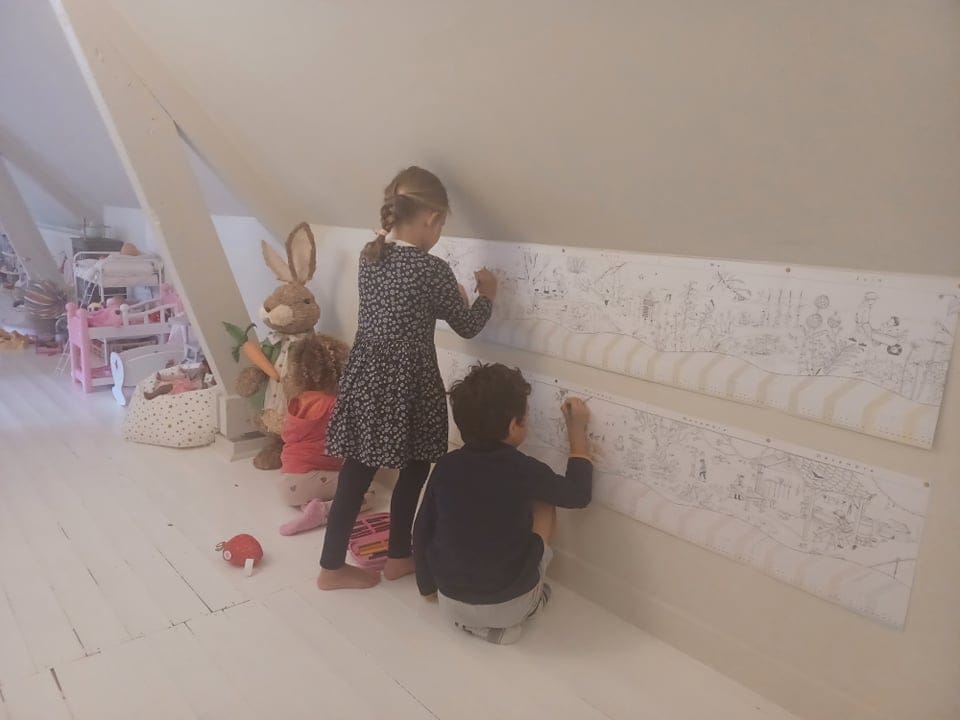Trois enfants colorient le Calendrier Panoramique affiché au mur
