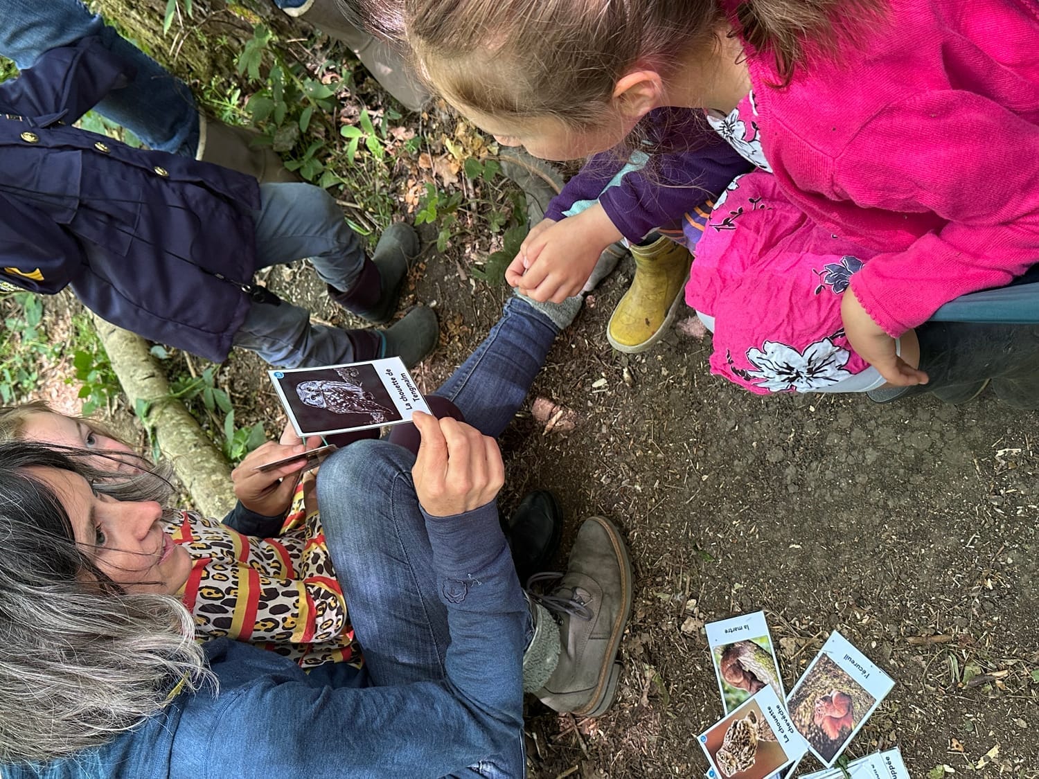 Laetitia montre la carte devinette de la Chouette de Tengmalm à une petite fille en forêt