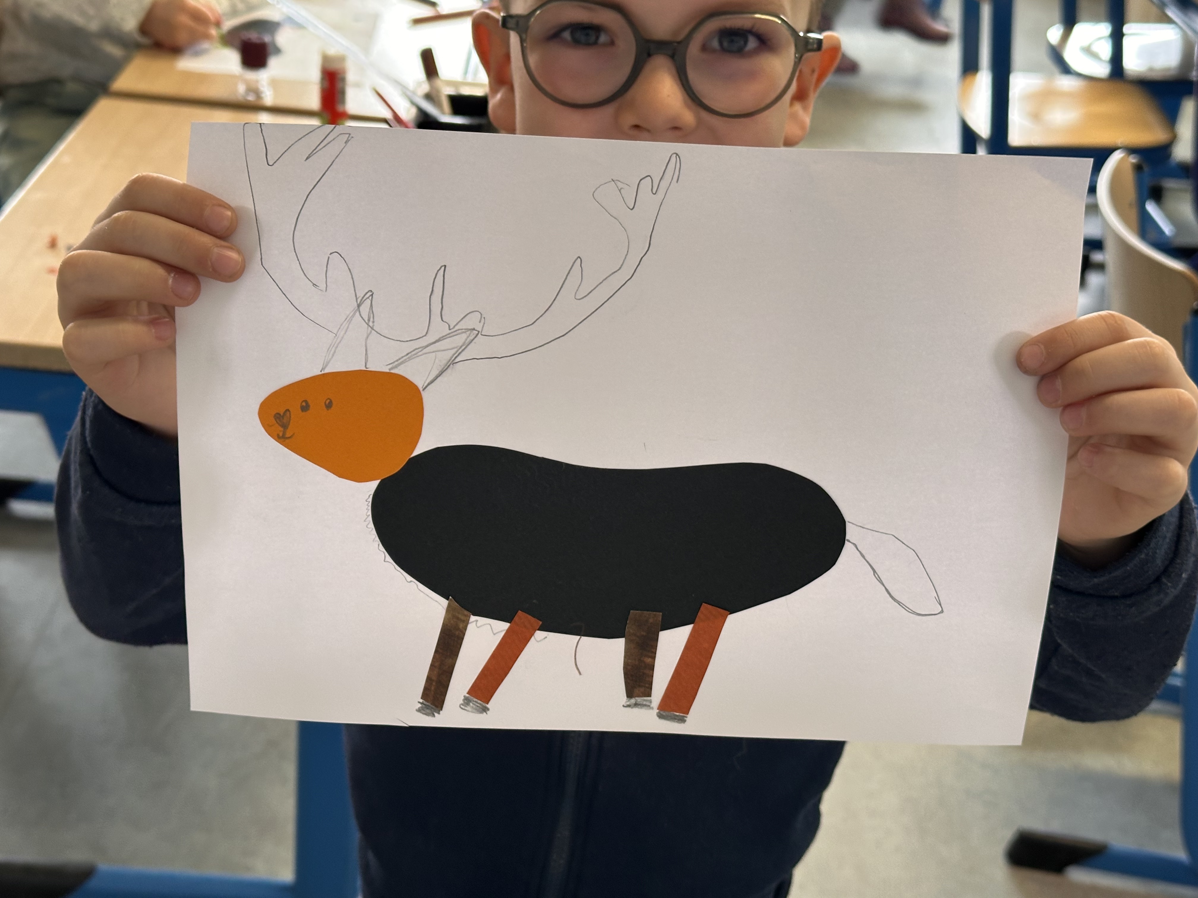 Un enfant du CSM tient son collage de cerf, seuls son regard et ses mains sont visibles