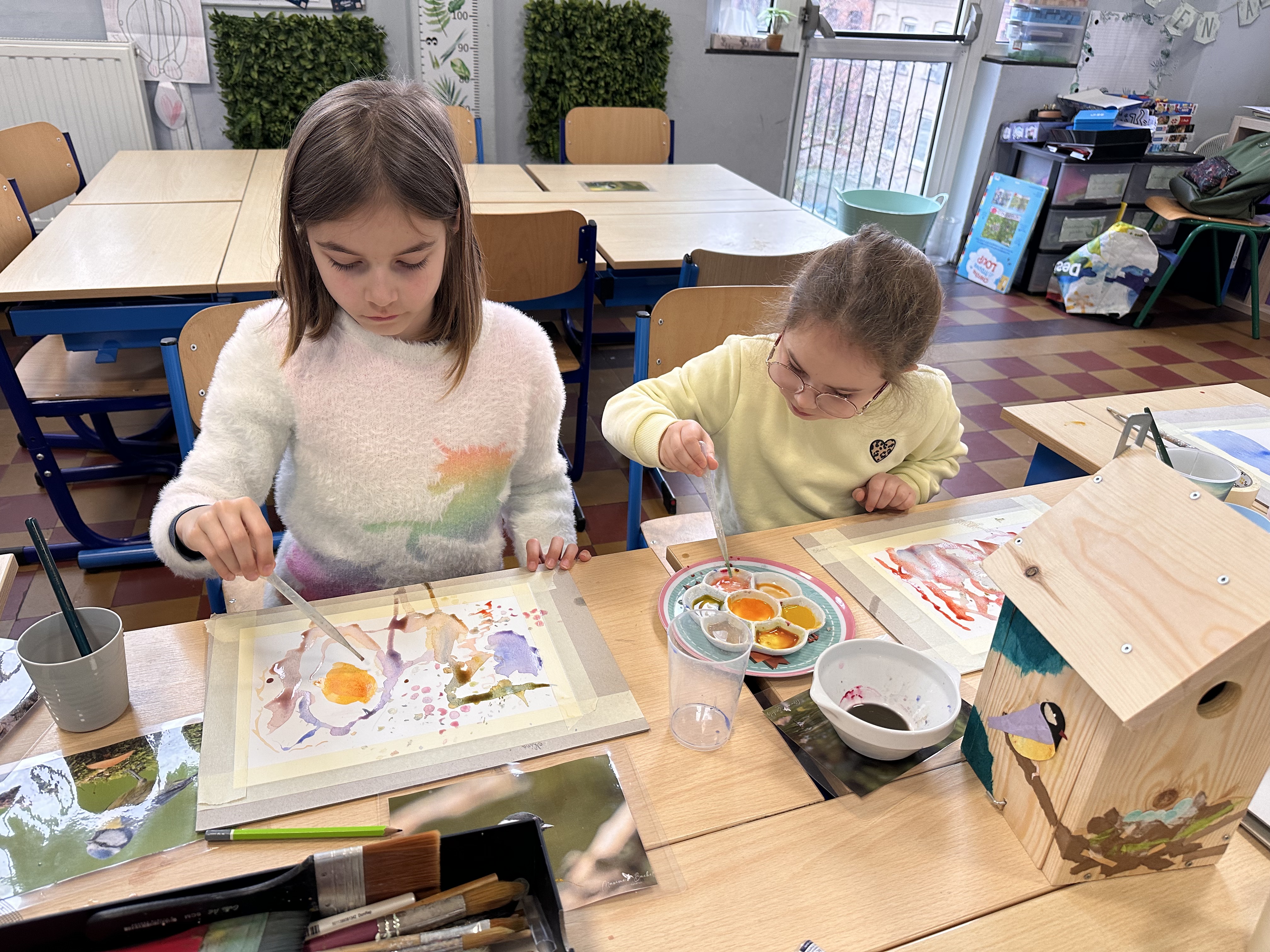 Deux filles de 2ème primaire au CSM colorant leur feuille d'aquarelle avec des pipettes à leur bureau