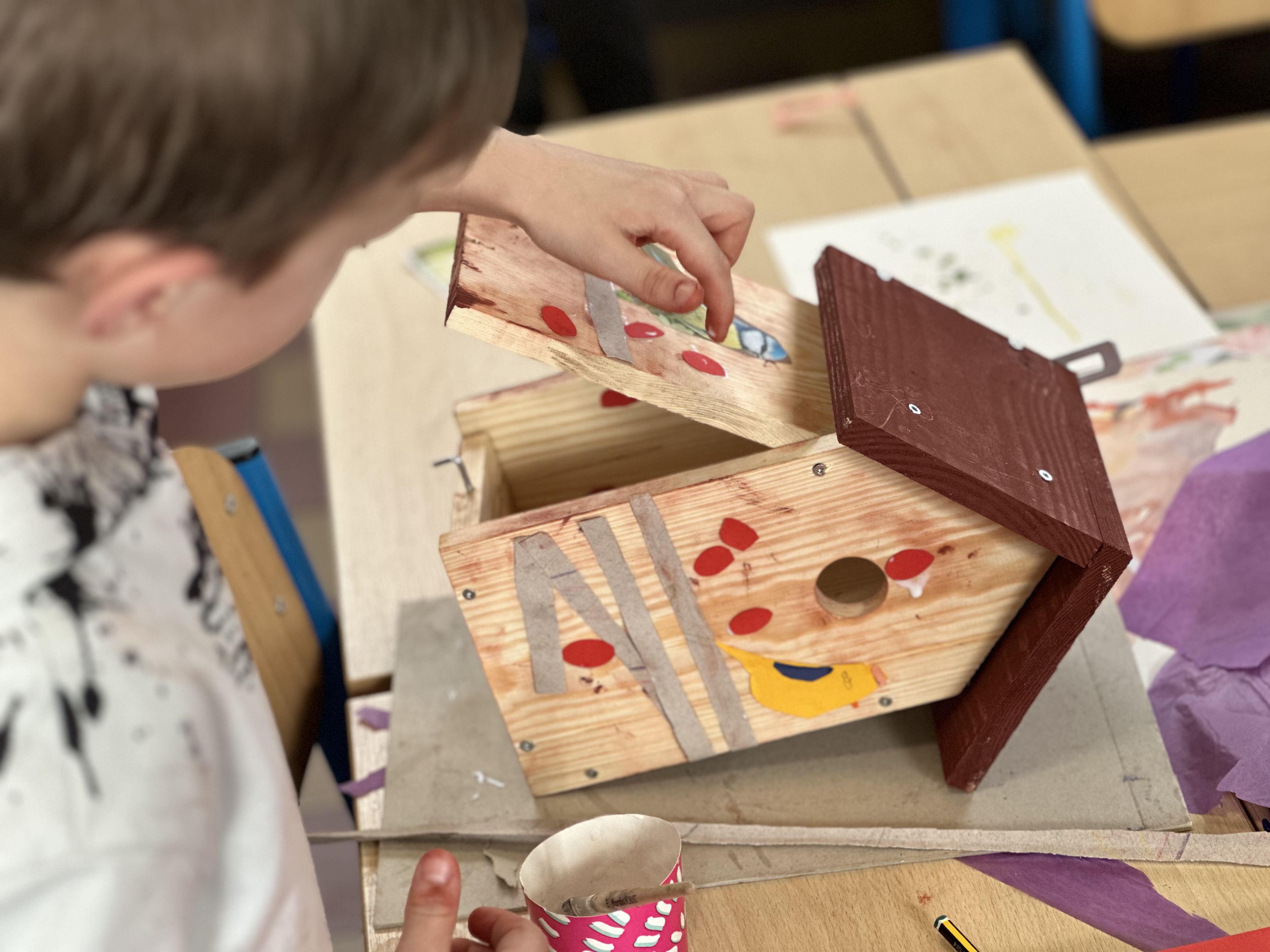 Petit garçon collant des œufs rouges en papier à l'intérieur de son nichoir, atelier CSM Mouscron