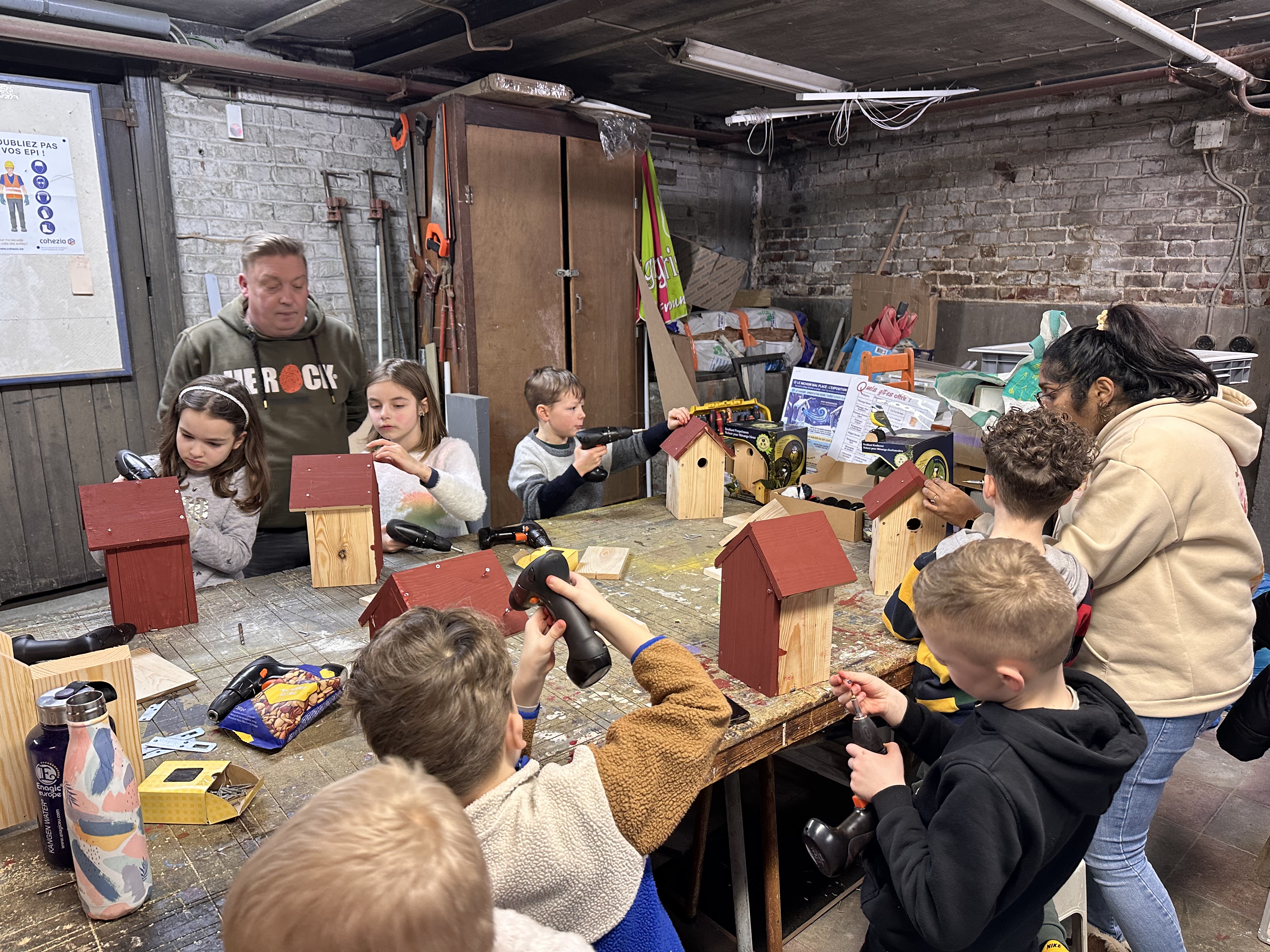 Les élèves de 2ème primaire du CSM assemblent les pièces de leurs nichoirs avec leur institutrice Caroline dans la salle de bricolage