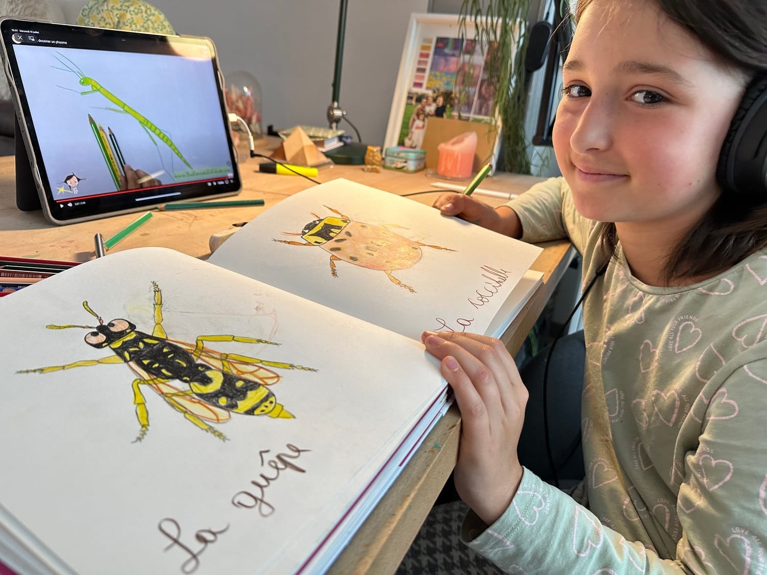 Céleste dessine dans son carnet avec la vidéo pas-à-pas sur le phasme en arrière-plan